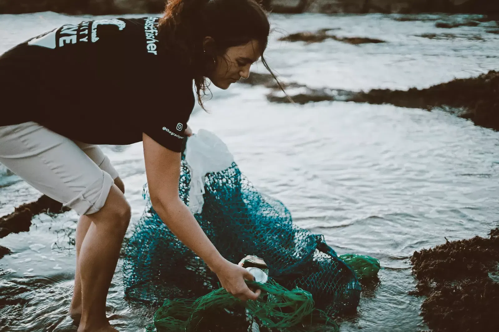 Immagine di una ragazza che raccoglie della plastica in mare